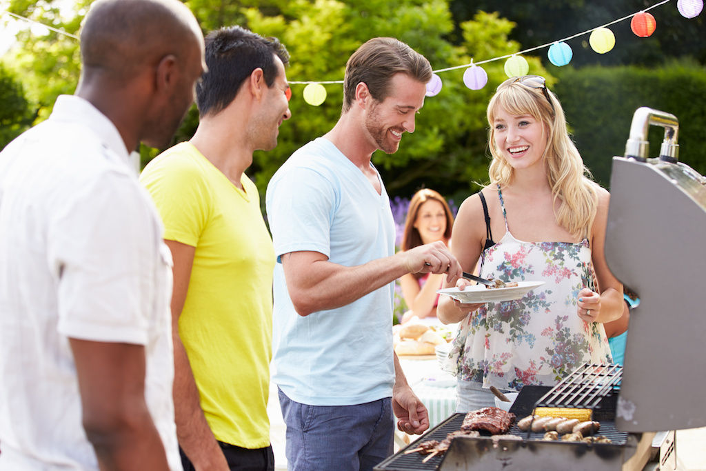 Four friends standing around barbecue grill